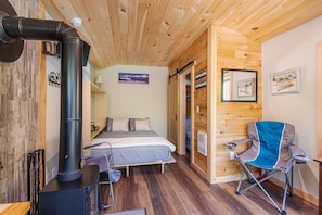 Ein Holzblockhaus-Interieur mit einem Bett, einem Sessel, einem Kamin und einer Holzbalkendecke.