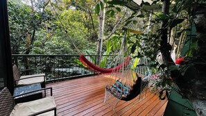 A wooden deck with a hammock, wicker furniture, and a view of dense greenery. - Monteverde Coati Jungle Bungalow (Monteverde)