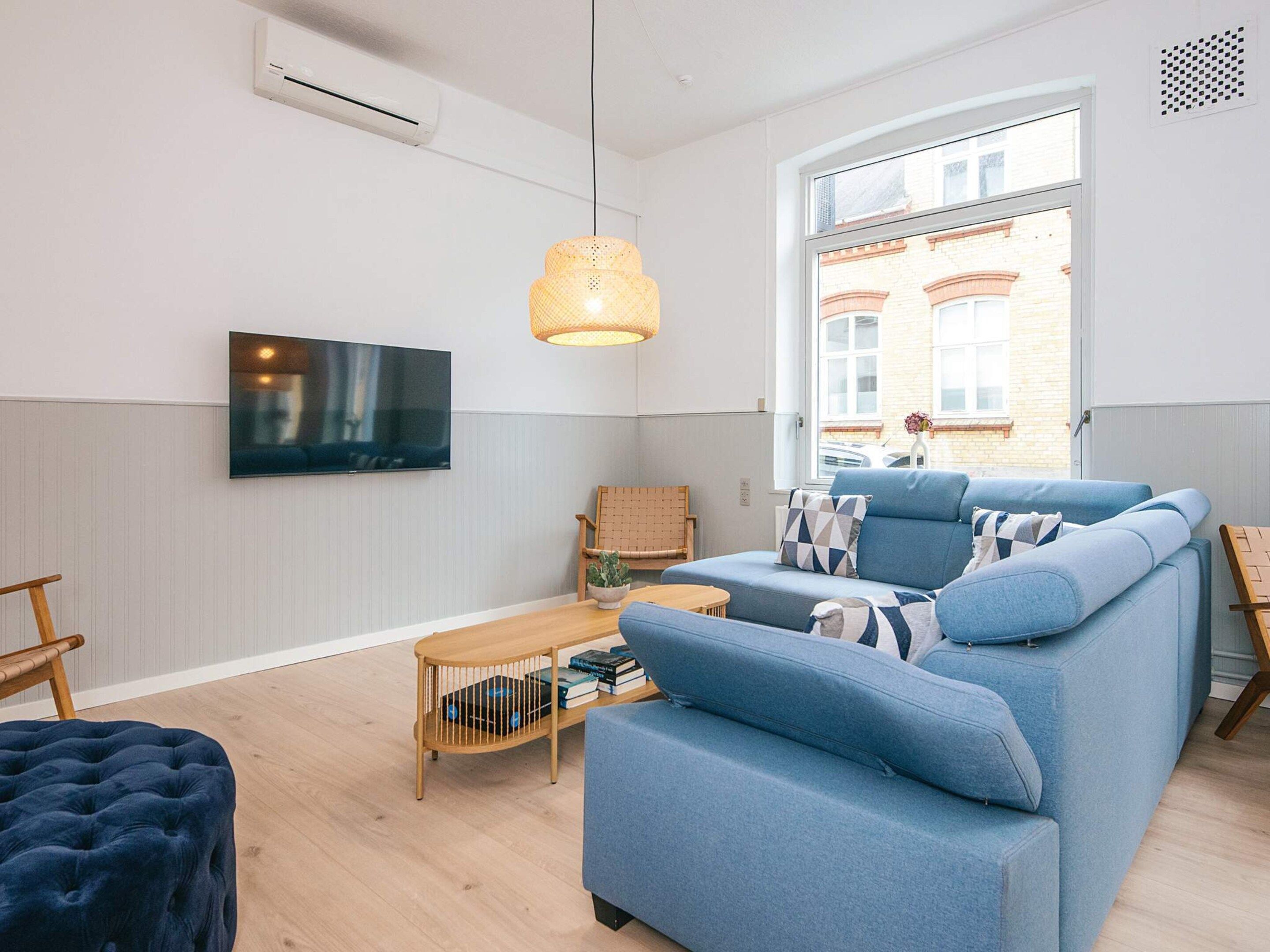 Una sala de estar moderna con un sofá azul, una mesa de centro de madera y un televisor montado en la pared.