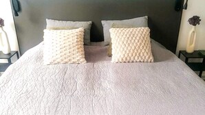 Una cama con un edredón blanco texturizado y dos almohadas cuadradas con un diseño texturizado.