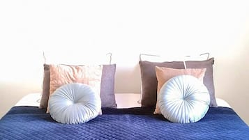 Una cama con colcha azul, dos almohadas y un cuadro colgado en la pared.