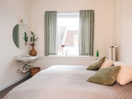 Ein Schlafzimmer mit einem Bett, einem Nachttisch, einem Spiegel, einem Fenster mit Vorhängen und einer Heizung.