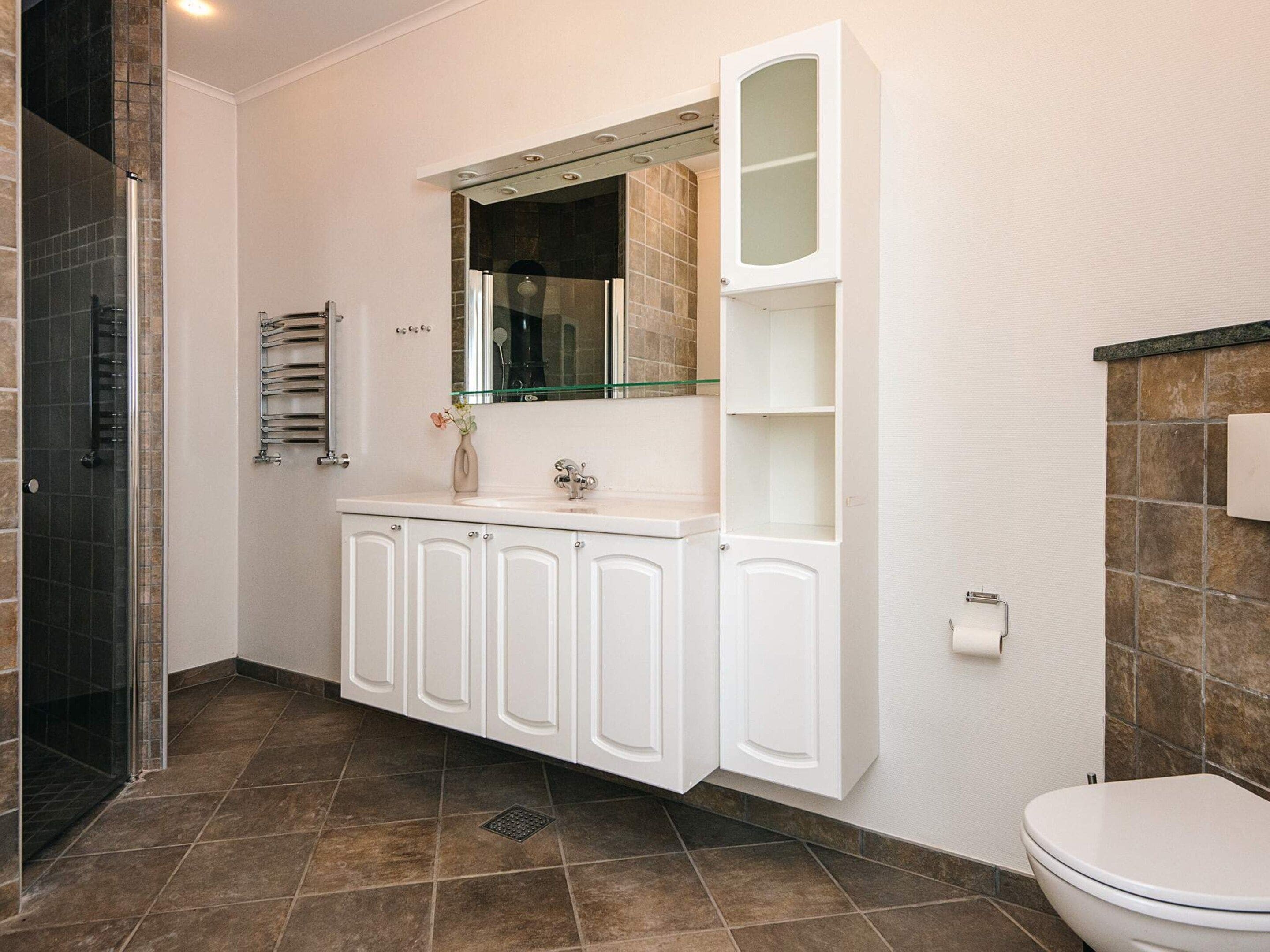 A bathroom with a white vanity, a mirror, a toilet, and a shower area.