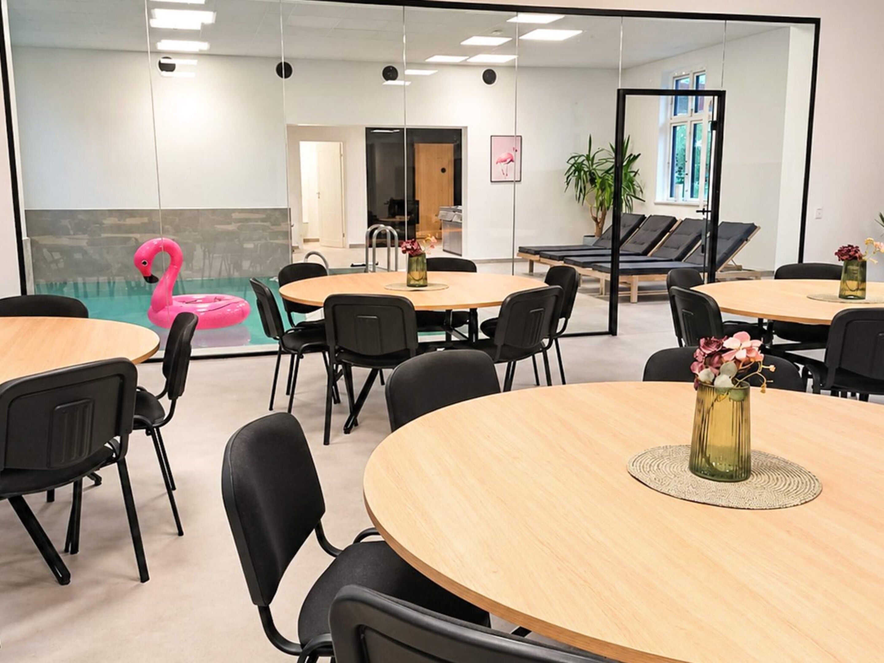 Une salle de conférence moderne avec des tables rondes, des chaises noires et un mur en verre.