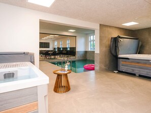 A modern indoor pool area with a lounge chair, a small table with a vase, and a poolside table. - 4 Star Holiday Home in Aabenraa (Aabenraa)