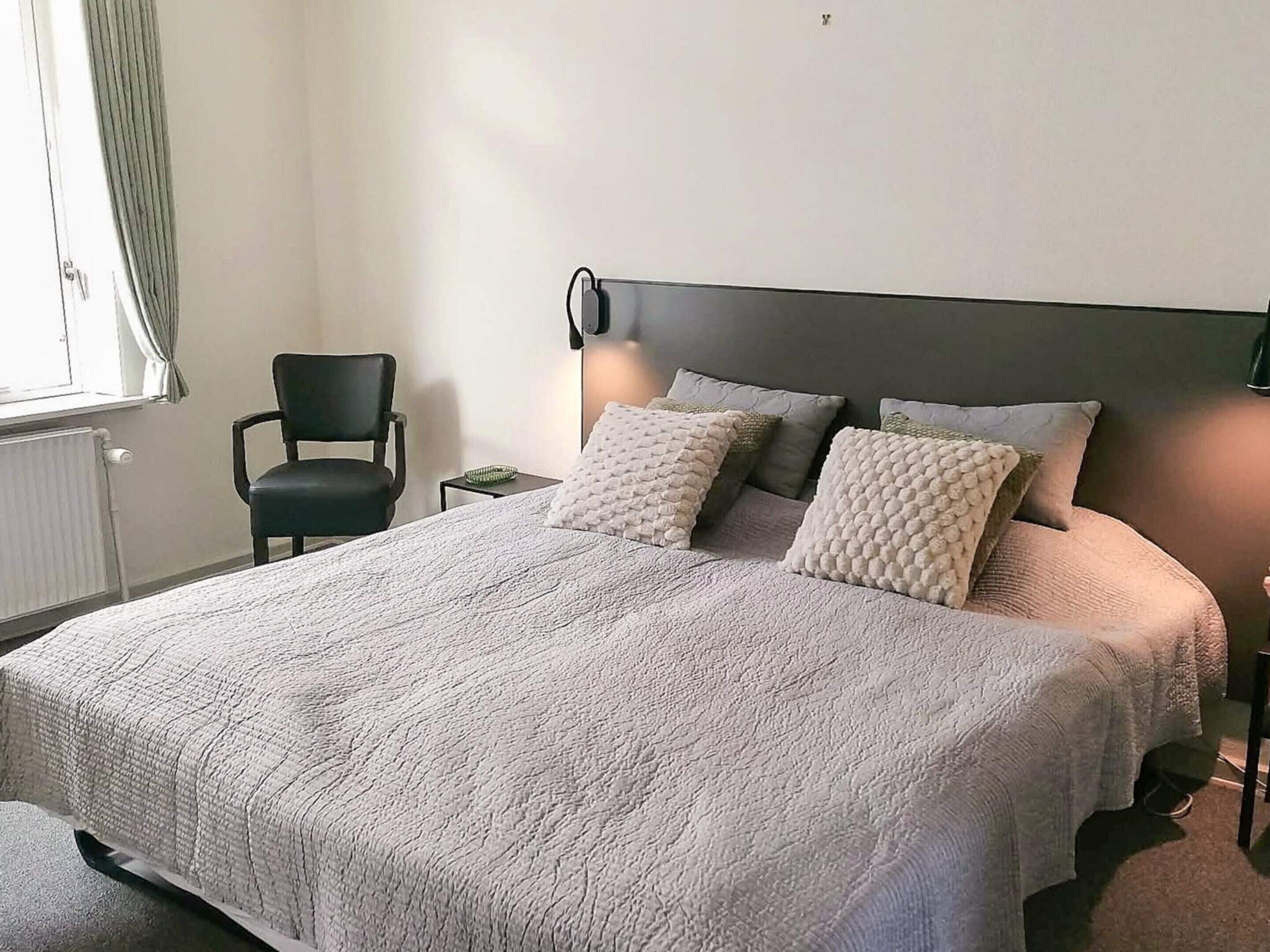 Quarto com cama, uma cadeira, mesa de cabeceira e abajur.