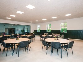 Un salón de conferencias con varias mesas y sillas, ventanas amplias y un techo alto con iluminación empotrada.
