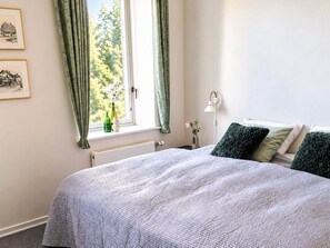 A bedroom with a bed, a window with curtains, a radiator, a bedside table with a lamp, and two framed pictures on the wall. - 4 Star Holiday Home in Aabenraa (Aabenraa)