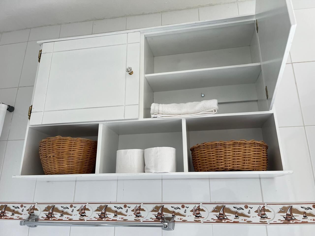 A bathroom with white cabinets, two wicker baskets, and two rolls of toilet paper.