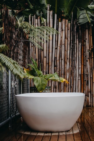A white bathtub in a bathroom with a bamboo fence and green plants in the background.. The black Yurt