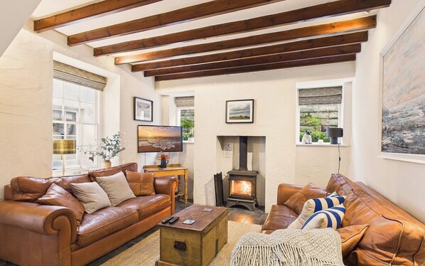 Ein gemütliches Wohnzimmer mit Ledersofas, einem Kamin, Holzbalken und Kunstwerken an den Wänden.