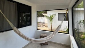 A hammock in a room with a view of a garden, a window, and a small stool. - Luxury Cabins with Private Cenote, Pool and A/C in the Jungle (AKUMAL)