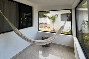 Eine Hängematte in einem Zimmer mit Blick auf einen Garten, ein Fenster und einen kleinen Hocker.