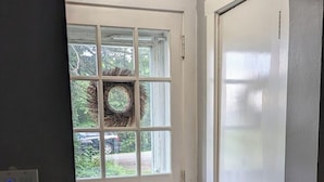 A hallway with a white door, a window with a wreath, and a ceiling light. - The Fairy Tale House - Minutes to PSU & Downtown - HOT TUB & FENCED IN YARD!! (State College)