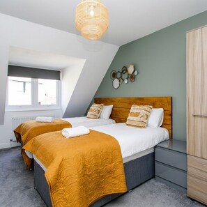 A modern bedroom with two beds, a wooden headboard, a grey dresser, and a unique wall art piece. - 198 Portland Apartments by Rizalina (Newcastle upon Tyne)