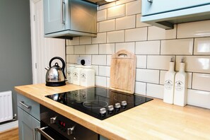 Een keuken met een zwarte inductiekookplaat, een waterkoker en twee flessen azijn.