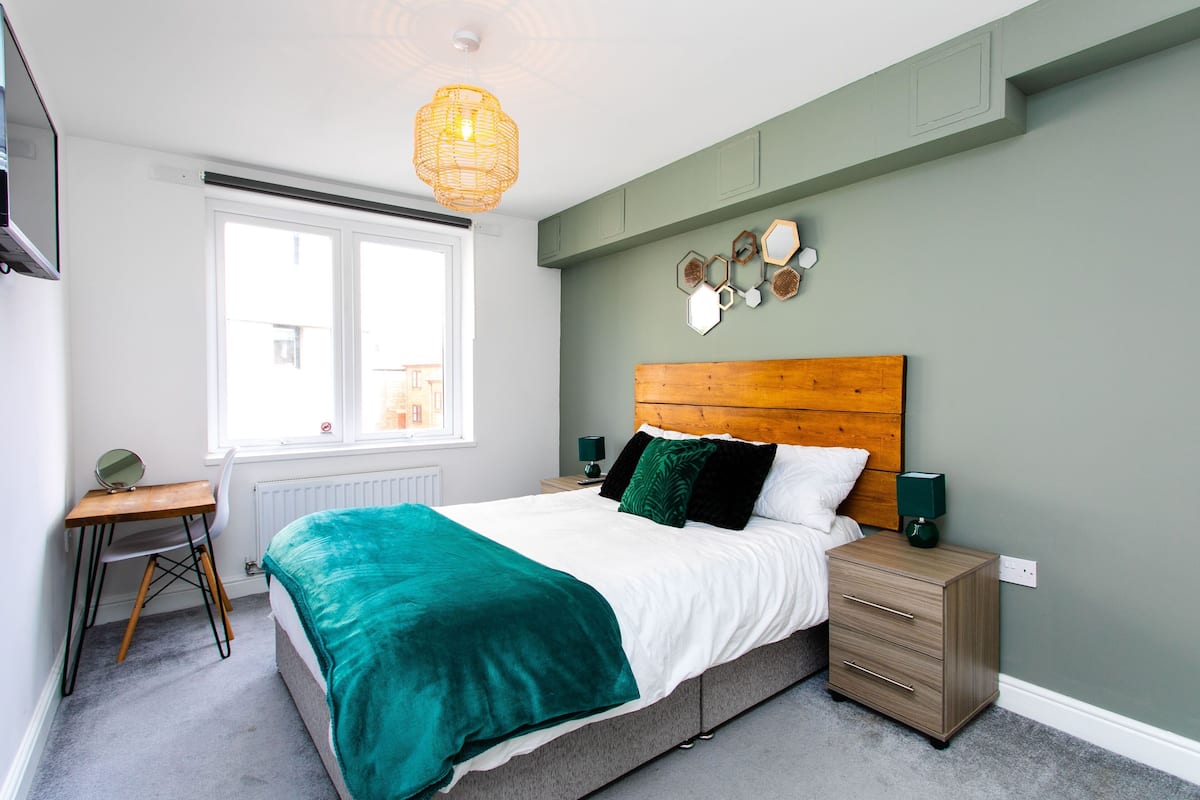 A bedroom with a bed, bedside table, lamp, and a window.
