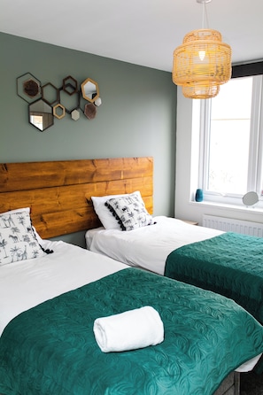 A hotel room with two beds, a wooden headboard, a large window, and a wall-mounted mirror. - 198 Portland Apartments by Rizalina (Newcastle upon Tyne)