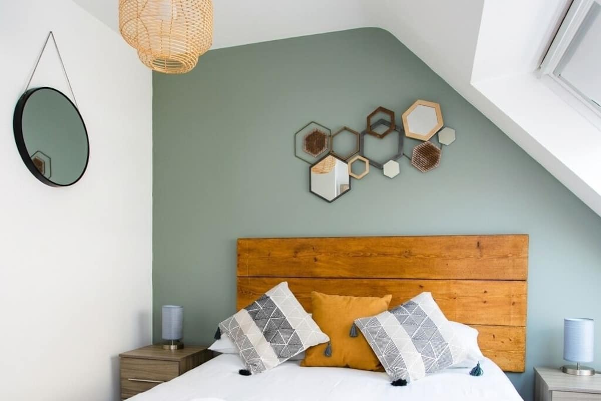A bedroom with a wooden headboard, a bed with white and yellow bedding, two bedside tables, and a wall-mounted mirror.