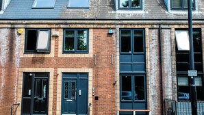 A two-story brick building with a black front door, a small window, and a bench outside. - 198 Portland Apartments by Rizalina (Newcastle upon Tyne)