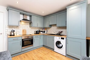 A compact kitchen with light blue cabinets, a built-in oven, a microwave, and a washing machine.