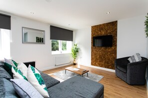 A modern living room with a sofa, a coffee table, a TV mounted on a textured wall, and a potted plant. - 198 Portland Apartments by Rizalina (Newcastle upon Tyne)