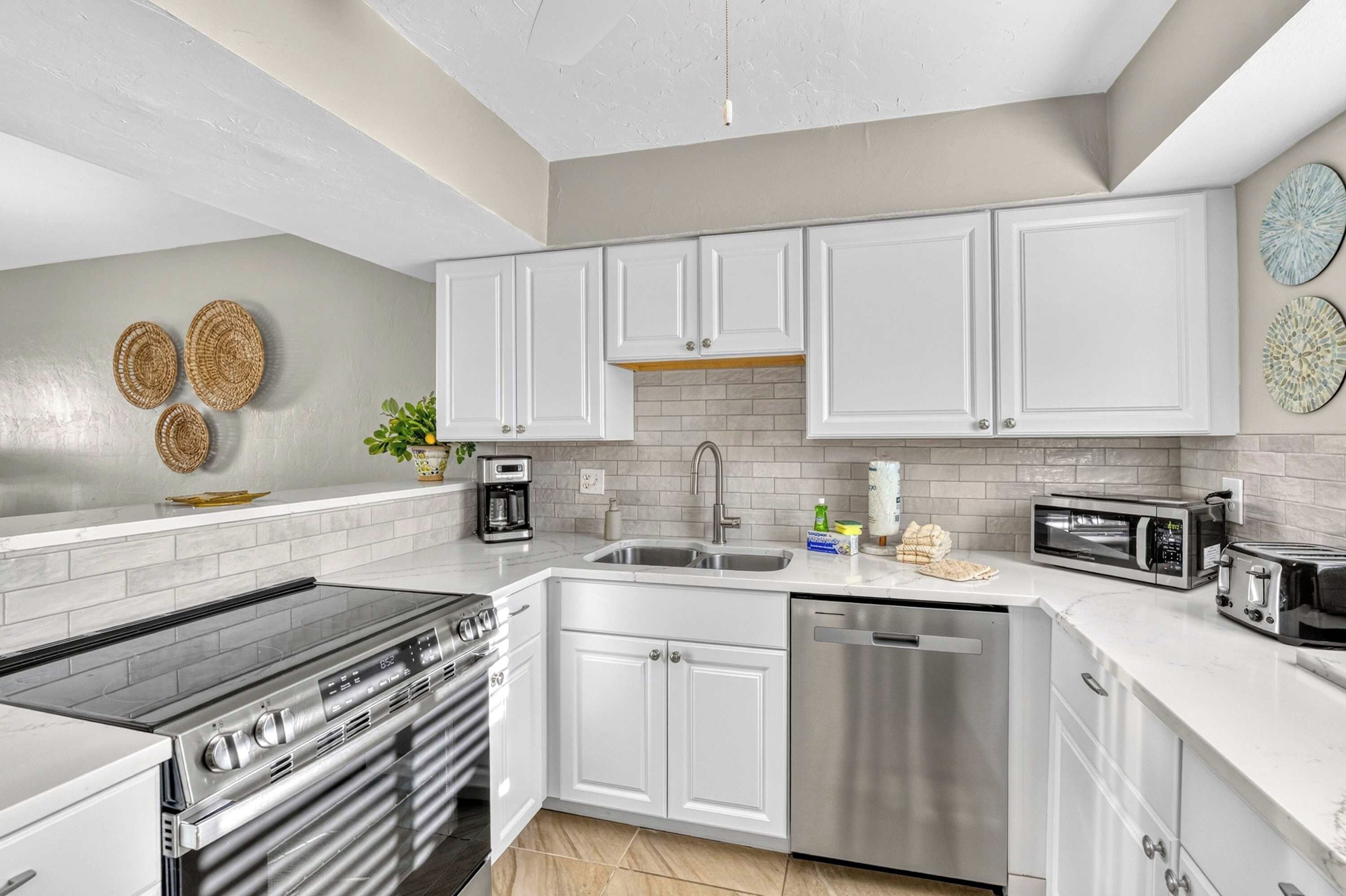 A modern kitchen with white cabinets, a stainless steel dishwasher, a built-in oven, a coffee maker, and a microwave.
