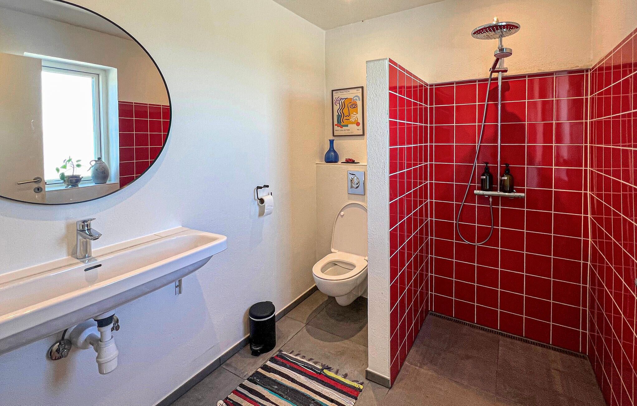 A bathroom with a white sink, toilet, and red-tiled shower enclosure.