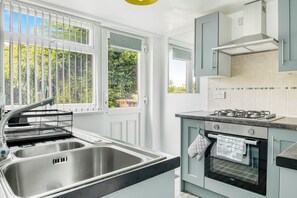 Une cuisine équipée d’un évier à deux bacs, d’une cuisinière et d’une fenêtre donnant sur un espace verdoyant.