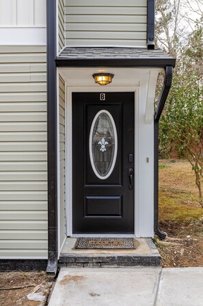 Uma porta frontal preta com um painel de vidro e um tapete de entrada, com uma luminária acima.
