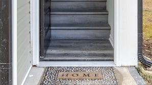 Una escalera que lleva a una puerta con un felpudo que dice 'HOGAR'.