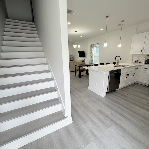 A modern kitchen with a central island, white cabinetry, and a staircase leading to another level. - New Construction 3-bedroom house in vibrant Houston (Houston)
