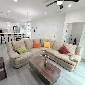 A modern living room with a sectional sofa, a wooden coffee table, and a kitchen in the background. - New Construction 3-bedroom house in vibrant Houston (Houston)