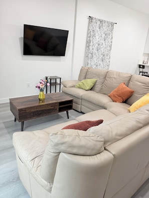 A living room with a sofa, a coffee table, a TV, and a floral curtain. - New Construction 3-bedroom house in vibrant Houston (Houston)