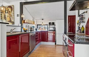 Eine moderne Küche mit roten Schränken, Holzboden und Blick in den Essbereich.