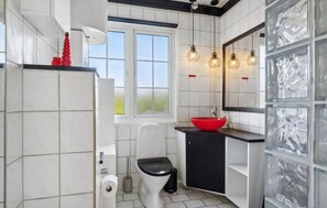 Ein Badezimmer mit weißen Fliesen, einer schwarzen Toilette, einem roten Waschbecken und einem Fenster mit Blick.