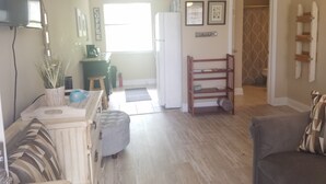 A living room with a sofa, a coffee table, a television, and a kitchen area with a refrigerator and a coffee machine. - Cozy studio condo in Biloxi. Walk to the beach! (Biloxi)