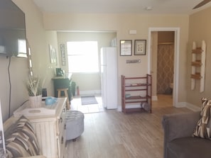 A living room with a sofa, a coffee table, a television, and a kitchen area with a refrigerator and a coffee machine. - Cozy studio condo in Biloxi. Walk to the beach! (Biloxi)