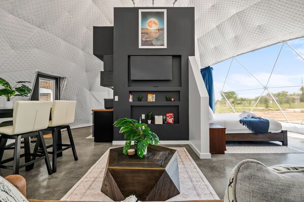 A modern living room with a large window, a sofa, a coffee table, and a wall-mounted TV.