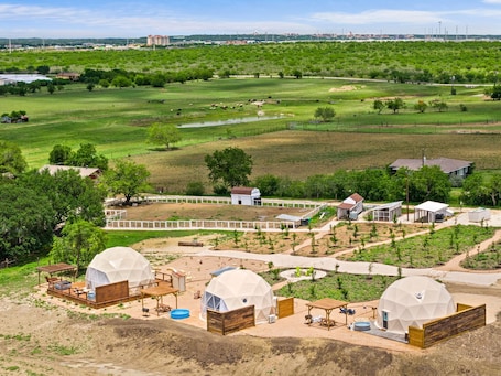 A large open field with a few buildings, including a white house and a barn, and several dome-shaped structures.. The Stargazer Glamping Dome with private hot tub