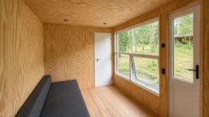 Una habitación pequeña con una banca, ventanas amplias y paredes de madera.