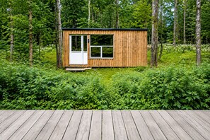 Eine Holzhütte mit Tür und Fenstern, umgeben von dichtem Grün.