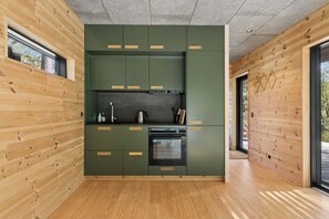 A modern kitchen with wooden walls, green cabinets, and a built-in oven. - Charming tiny house in forest near sea peace now (Hasle)