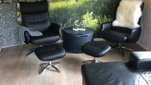 A room with a large window, a black leather sofa, a black leather armchair, and a small round table with a white furry throw. - Family holiday home with water park access (Oksbøl)