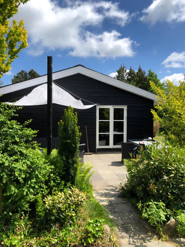 Ein Haus mit dunkler Fassade, einer weißen Tür und einer überdachten Terrasse.