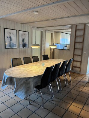 A conference room with a long table, black chairs, pendant lights, framed artwork, and a visible kitchen area. - Lovely pool house near the North Sea (Nørre Nebel)