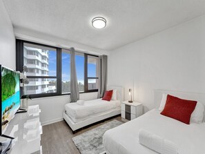 A hotel room with two beds, a TV, a desk, and a window with a view of buildings. - Ocean View Miami Beach Gem Beachfront Resort 606 (Miami Beach)