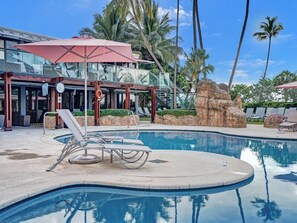 A swimming pool with lounge chairs, a lifebuoy, and a building with glass windows and a red umbrella. - Ocean View Miami Beach Gem Beachfront Resort 606 (Miami Beach)