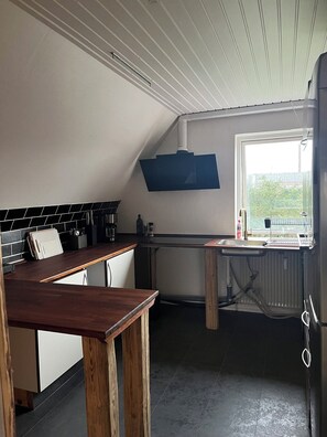 Et køkken med et træbord, hvide skabe, en sort backsplash og en blå væghængt hylde.