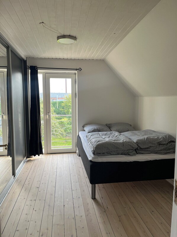 Et soveværelse med en seng, en skydedør til en balkon og trægulv.
